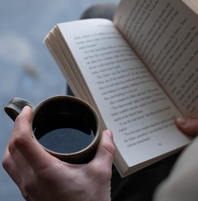 A coffee subscription customer enjoying a cup of freshly brewed Lost Horizon Coffee whilst reading a book